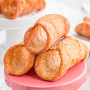 A stack of cannoli shells on a pink plate.