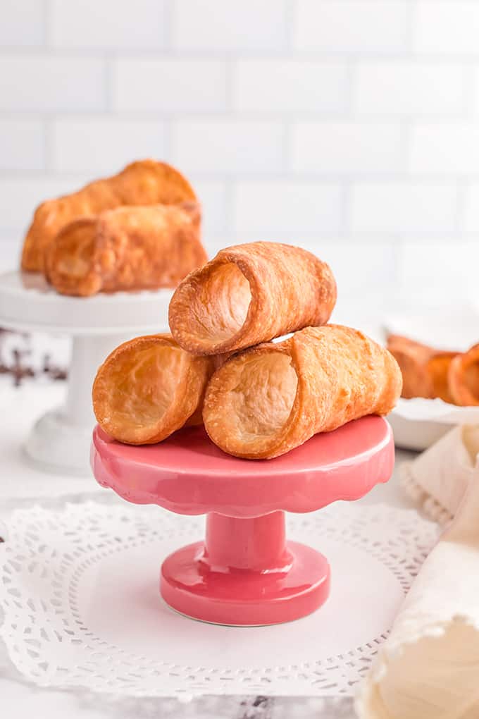 empty cannoli shells sitting on pink and white cupcake stands with doilies under them