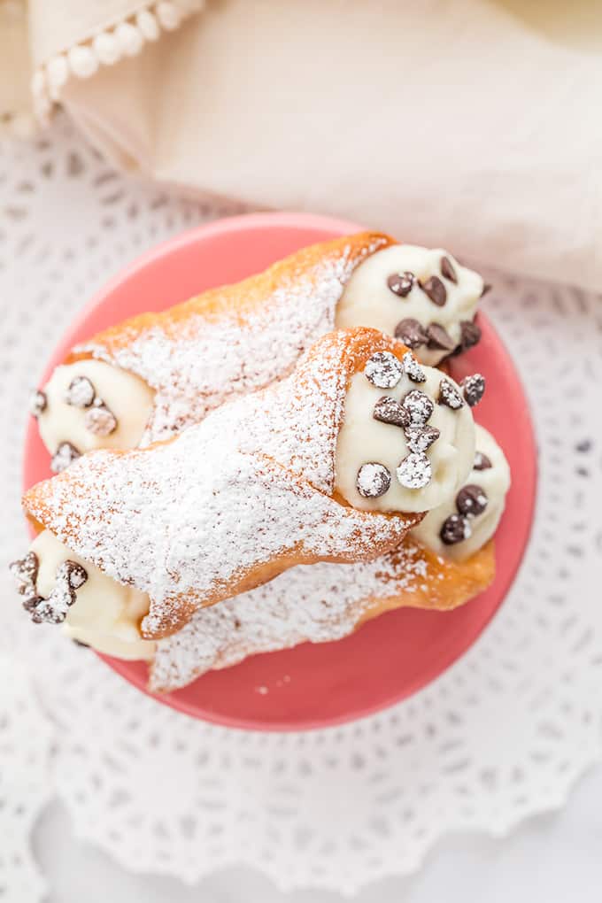 overhead photo of filled cannoli shells on a pink stand with a doilie under it