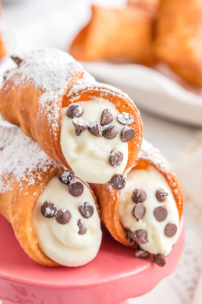 close up of cannoli shells with cream filling and mini chocolate chips on a pink cupcake stand