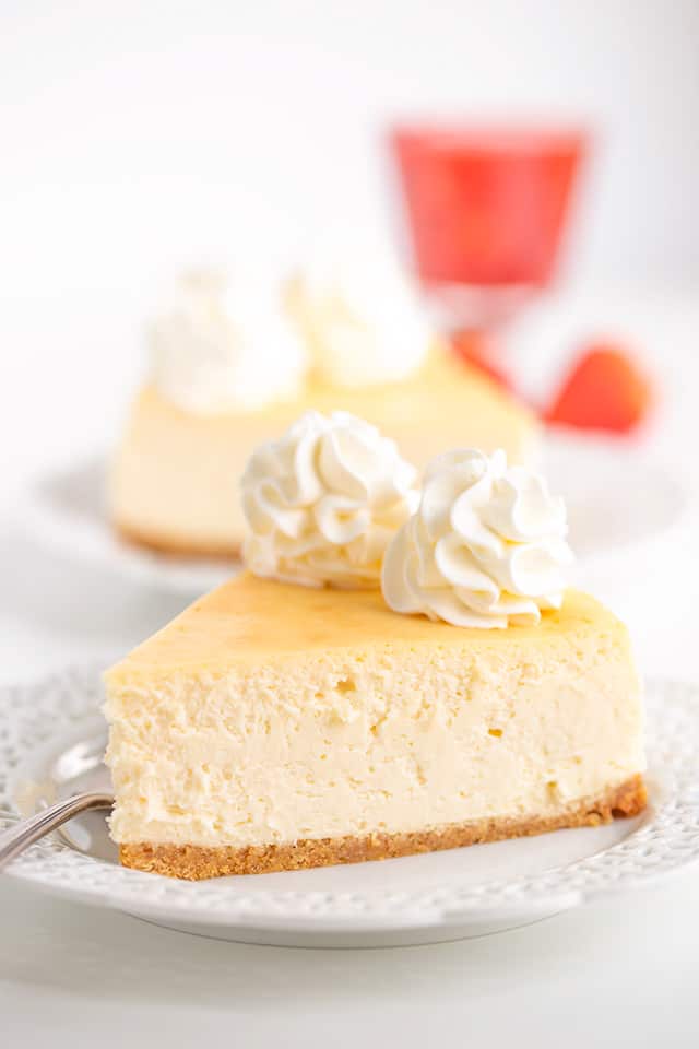 plain cheesecake on a white plate with strawberry sauce behind the plate