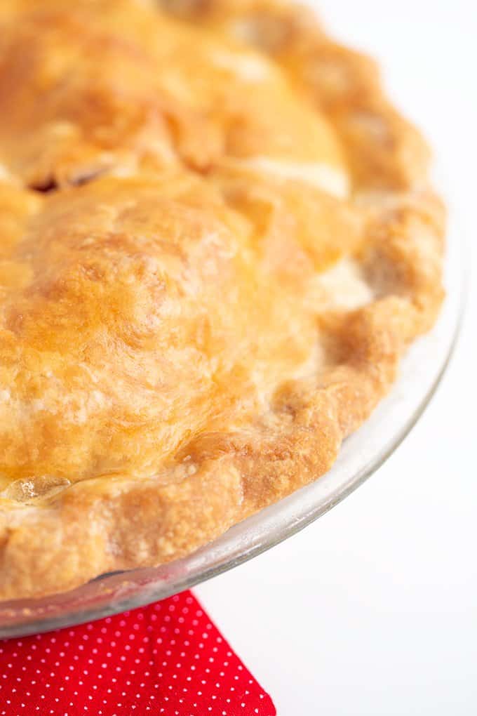 picture focusing on the edge of the crust of a pie on a white surface with a red fabric