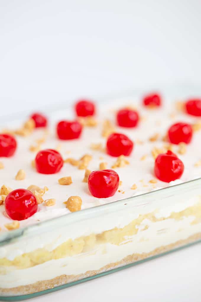 a glass pan full of a dessert with the layers showing on the side of the pan and the maraschino cherries in focus