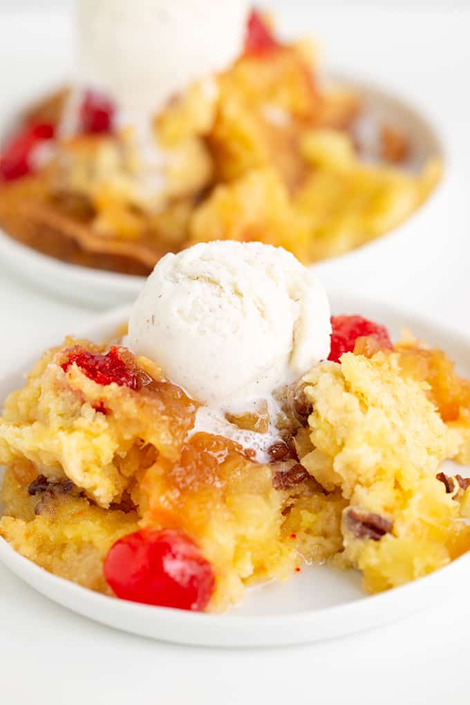 close up of the pineapple dump cake after it's been scooped onto a dessert plate with a scoop of ice cream on top