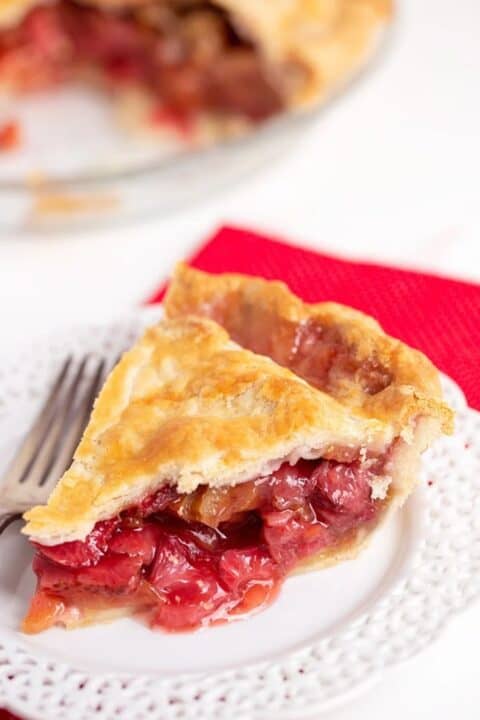 A slice of strawberry rhubarb pie on a white plate with a fork.
