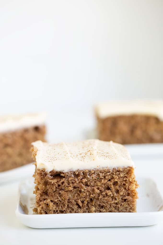 close up of a slice of zucchini cake on a white plate with other slices of cake behind it