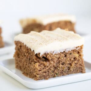 Square image of a zucchini cake on a white dessert plate on a white surface