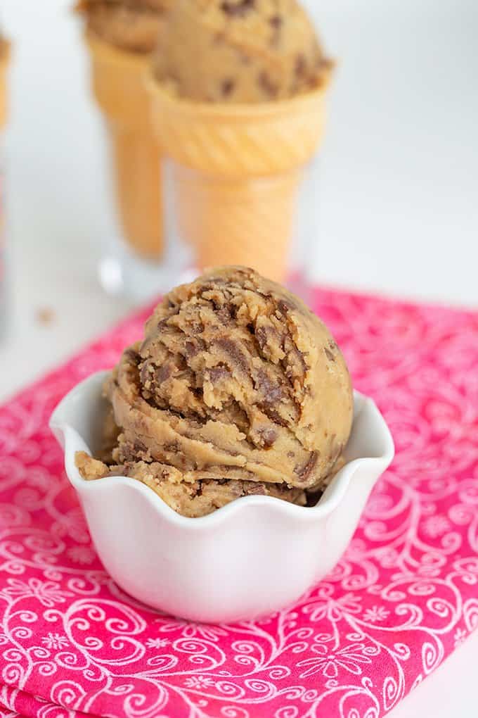 white bowl full of edible cookie dough on a bring pink fabric with a white background