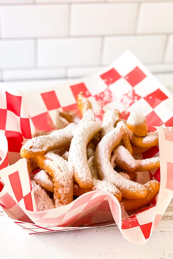 powdered sugar dusted funnel cake fries in a red and white checked wax paper