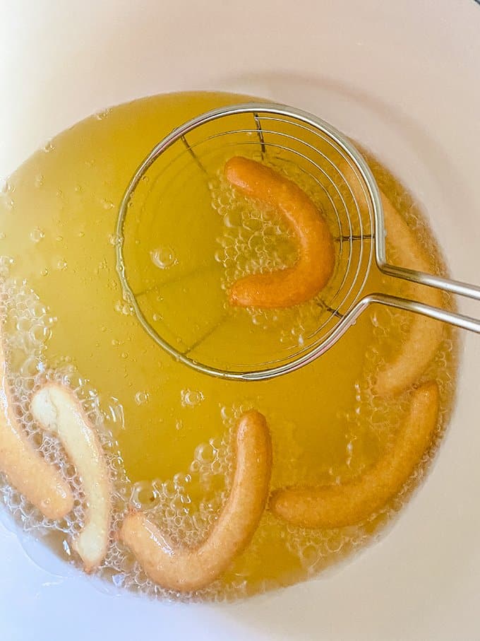 funnel cake fries in oil with a spider spatula scooping the fries out