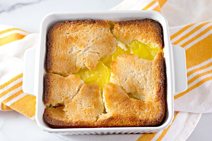 lemon cobbler in a white square baking dish with a white and yellow towel under the cobbler