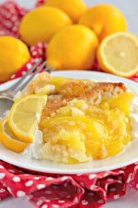 upclose picture of lemon cobbler on a white plate with fresh lemon slices and a fork