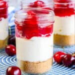 close up of a jar of cheesecake with cherries around the jar and a blue placemat underneath