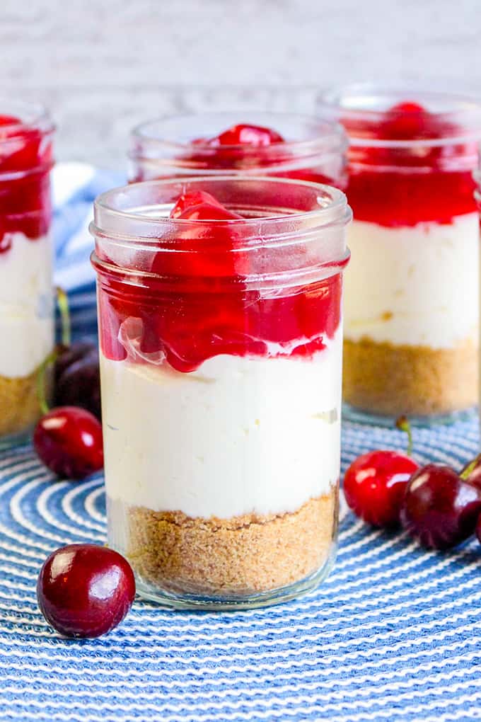 close up of a jar of cheesecake with cherries around the jar and a blue placemat underneath