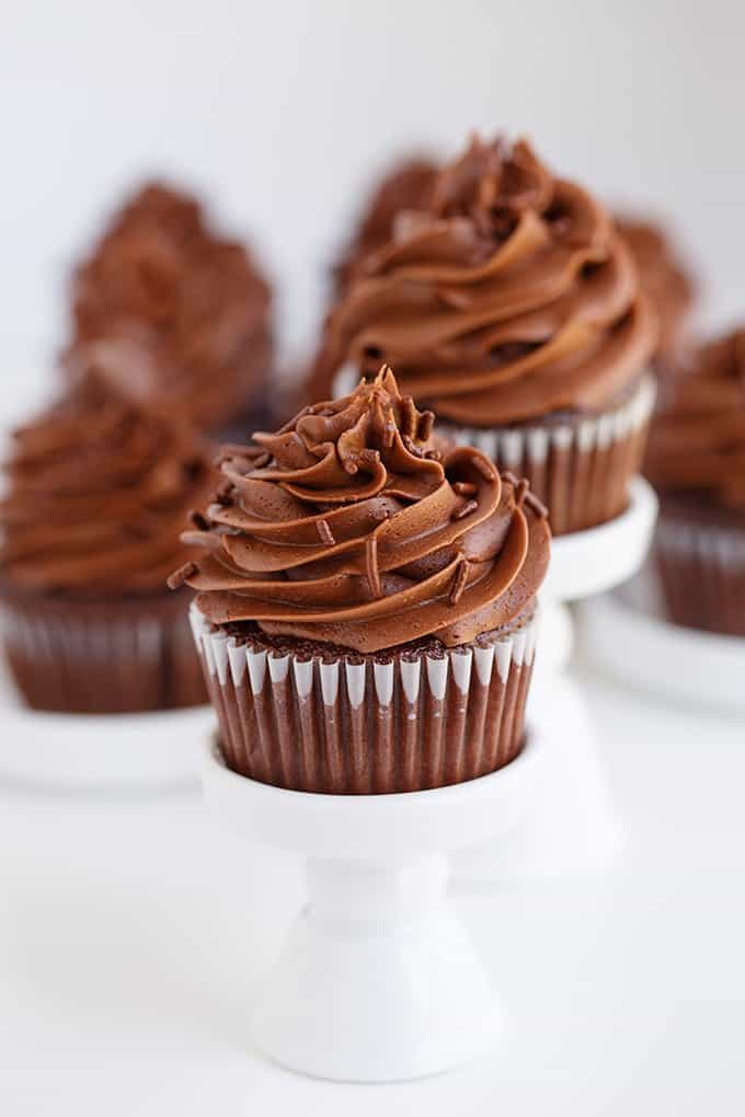 chocolate cupcakes on small white cupcake stands on a white surface