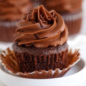 square image of an unwrapped chocolate cupcake on a white plate with chocolate frosting and chocolate sprinkles
