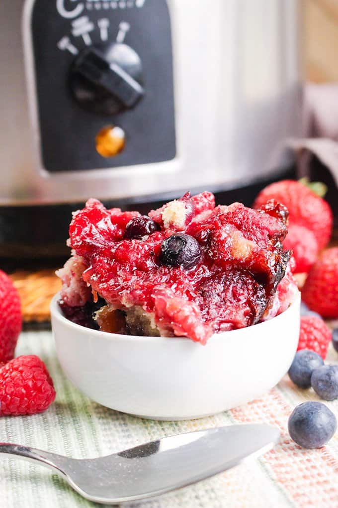 white bowl of berry cobbler with a spoon in front of it and fresh berries around it