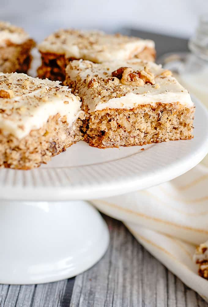 banana bars on a white cake plate with a yellow striped towel next to it