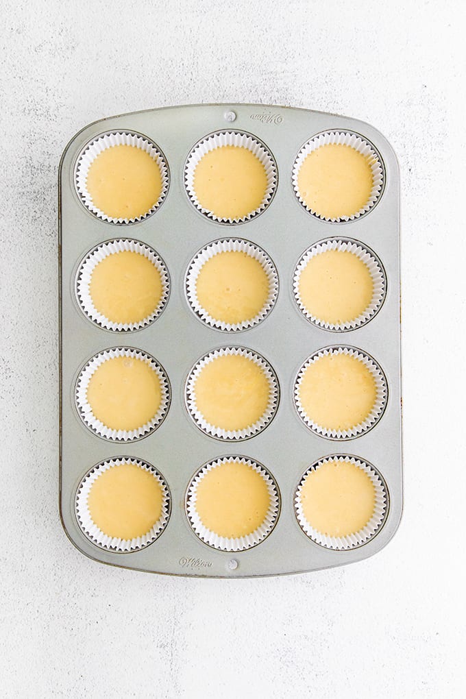 Cupcake pan with paper liners and cake batter in it on a gray surface