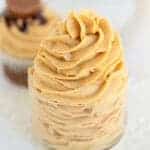 square image of swirled peanut butter frosting in a glass bowl on a white surface and a cupcake behind it