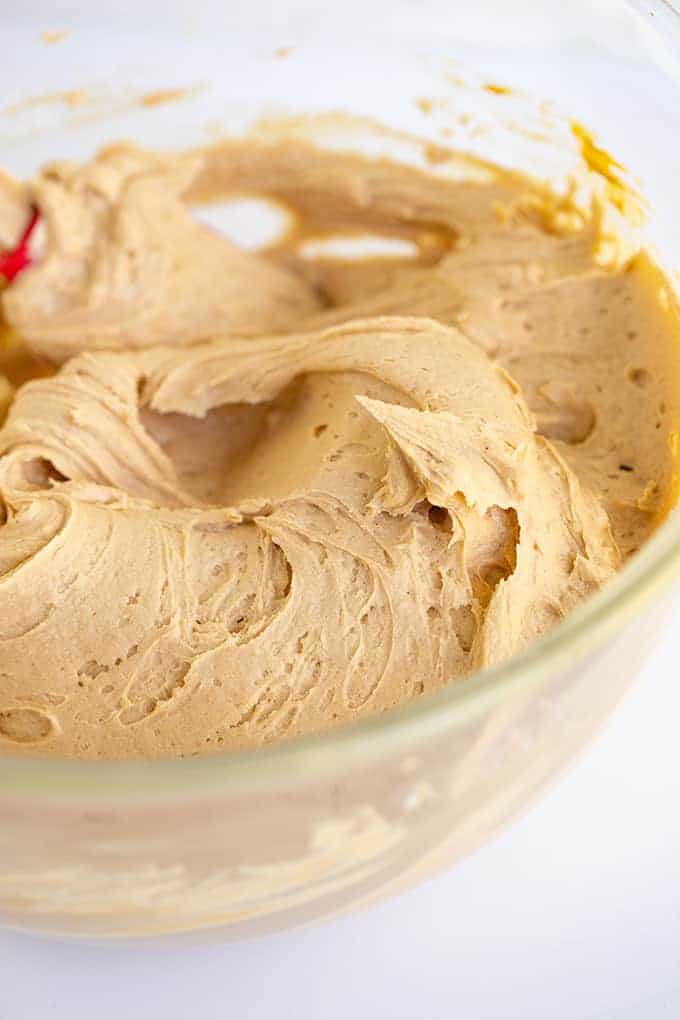 a glass bowl full of peanut butter frosting on a white surface