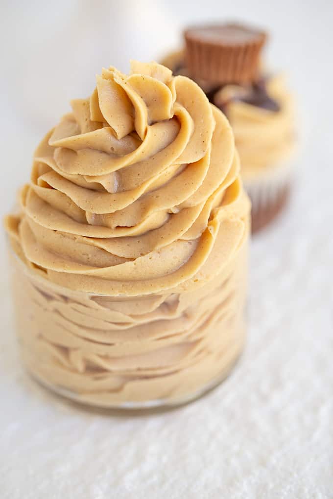 frosting swirled high in a small glass bowl with a cupcake behind it on a white surface