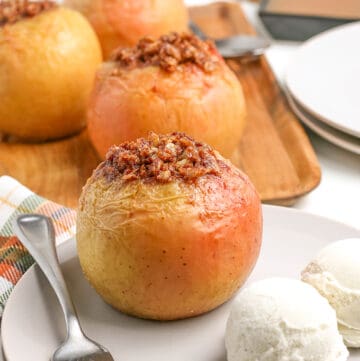 side view of baked apple on a white plate with a fork and two scoops of vanilla ice cream