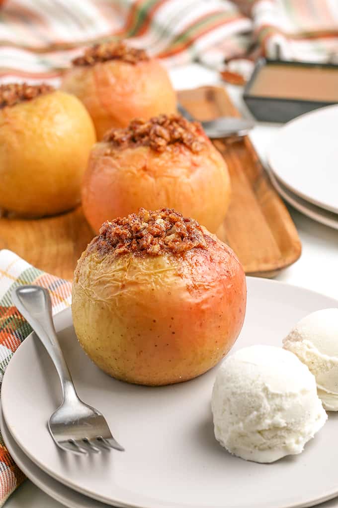 side view of baked apple on a white plate with a fork and two scoops of vanilla ice cream