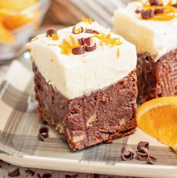 a piece of brownie on a gray plaid plate with orange slices and chocolate curls around it