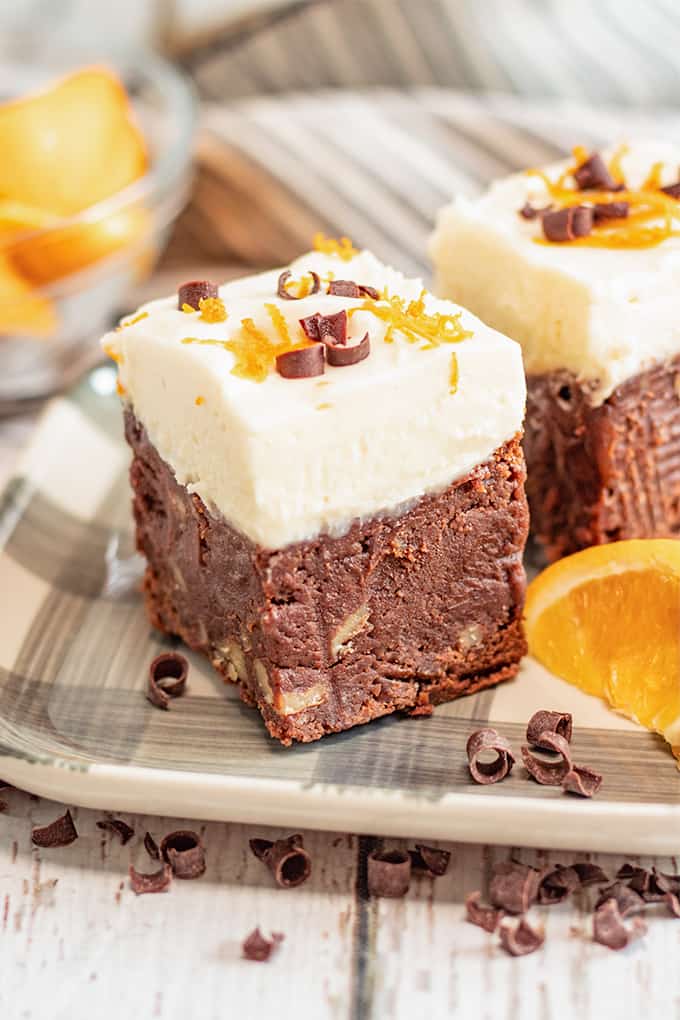 a piece of brownie on a gray plaid plate with orange slices and chocolate curls around it