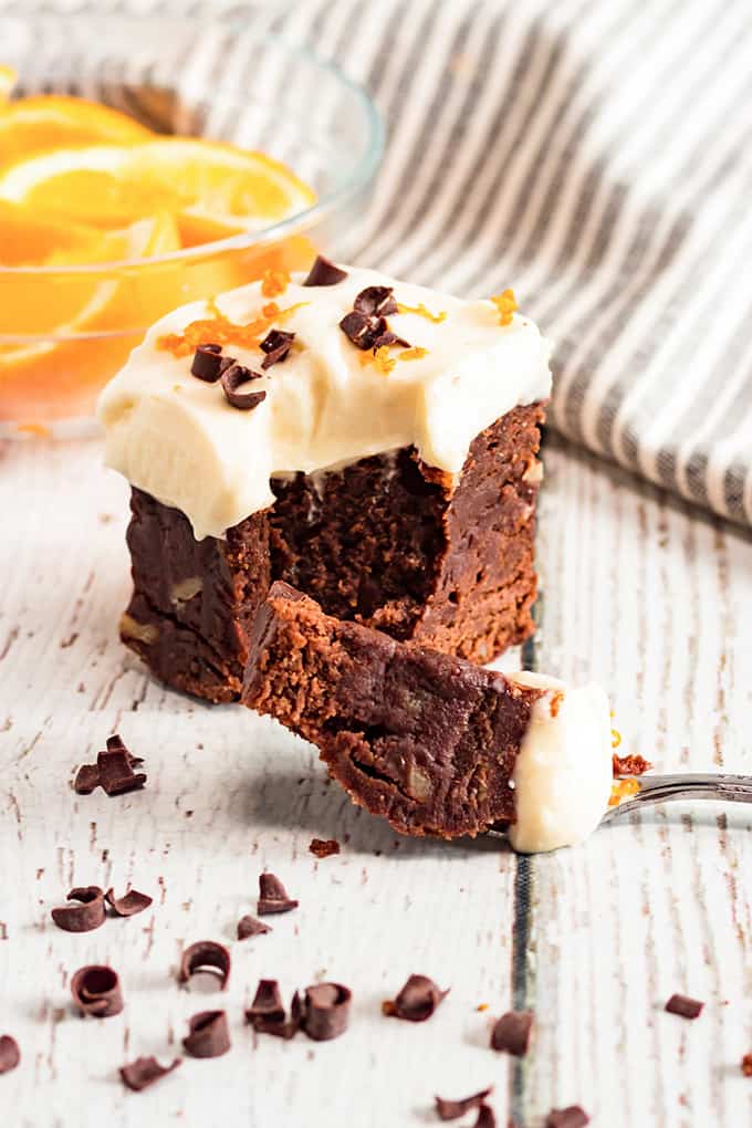 a brownie on the wooden surface with a fork full of brownie sitting in front of it and chocolate curls scattered