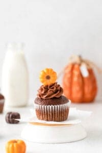 cupcake on an upside down white dish with a glass of milk and a pumpkin behind it