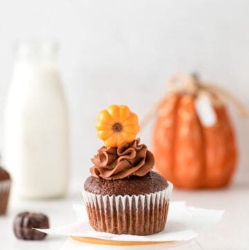 cupcake on an upside down white dish with a glass of milk and a pumpkin behind it