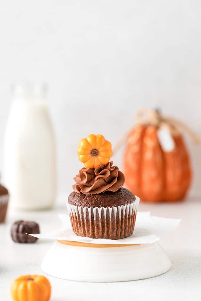 cupcake on an upside down white dish with a glass of milk and a pumpkin behind it