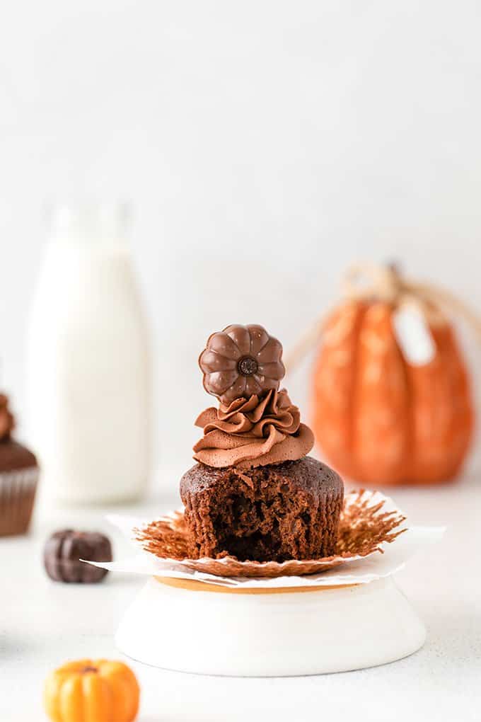 a cupcake that's unwrapped with a bite taken out of it with pumpkin truffles around it and a glass of milk