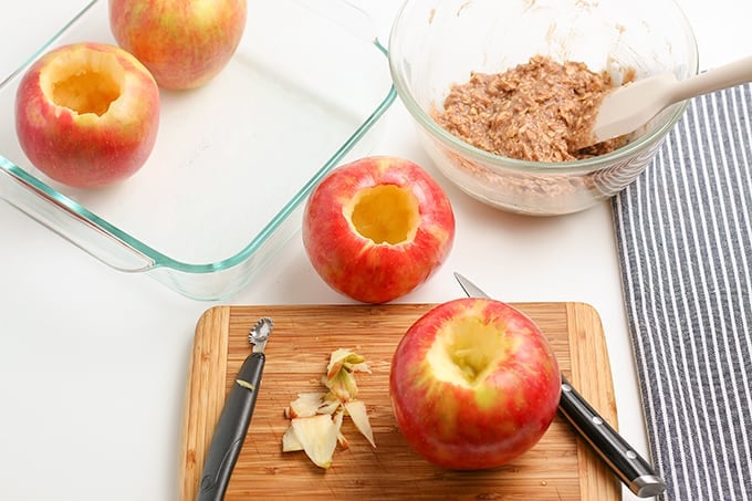 horizontal image of an apple on a cutting board with a knife and corer with a glass baking dish beside it and a striped linen