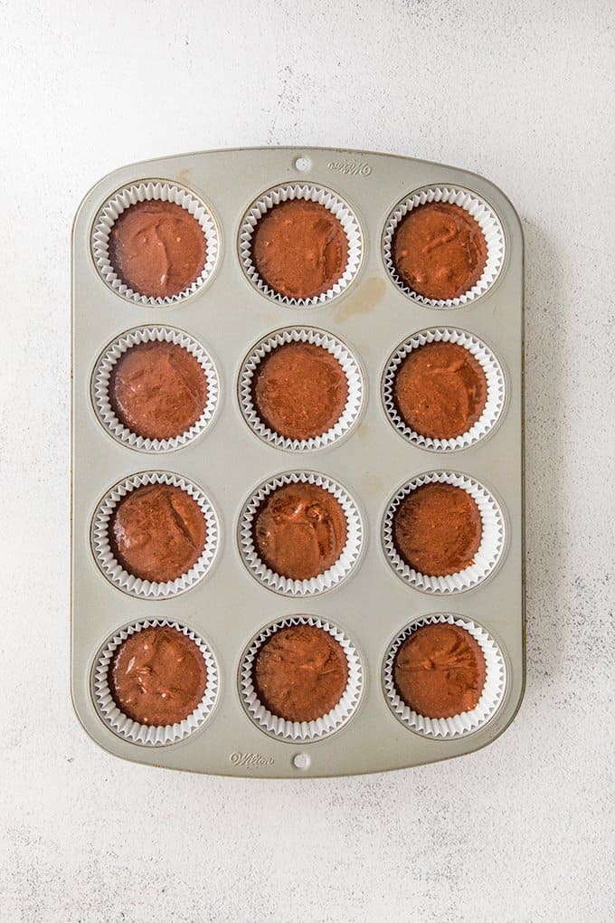 cupcake pan with paper liners filled with cake batter on a light colored surface