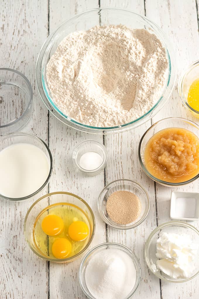 overhead photo of applesauce dinner roll ingredients in glass bowls on a white wood background