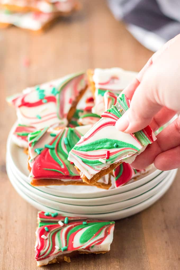 holding a piece of toffee in front of the stack of white plates