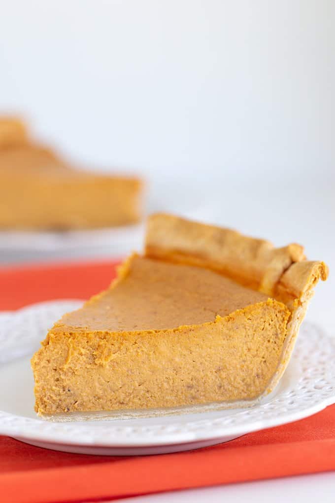 close up of a slice of cheesecake on a white plate with an orange linen under it