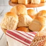 brown basket with a red and white linen full of dinner rolls with a cake plate full of applesauce rolls behind it