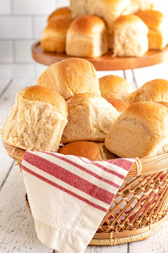 brown basket with a red and white striped linen full of applesauce rolls with a cake stand behind it full of dinner rolls