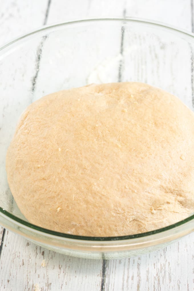 dinner roll dough in a large glass bowl on a white wooden surface