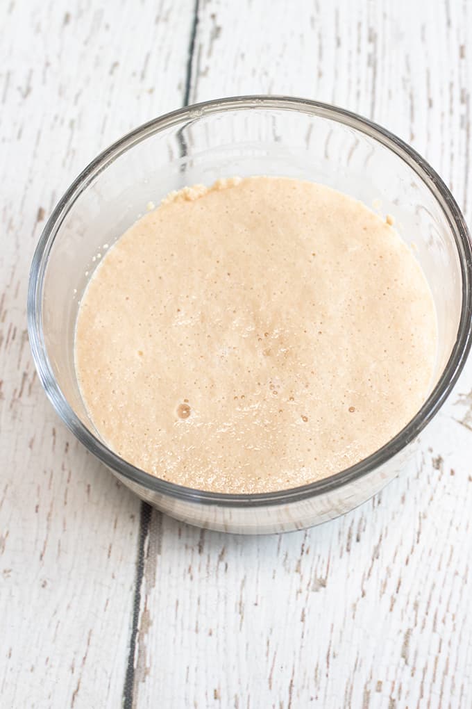 glass bowl full of yeast, sugar, and water on a white wood