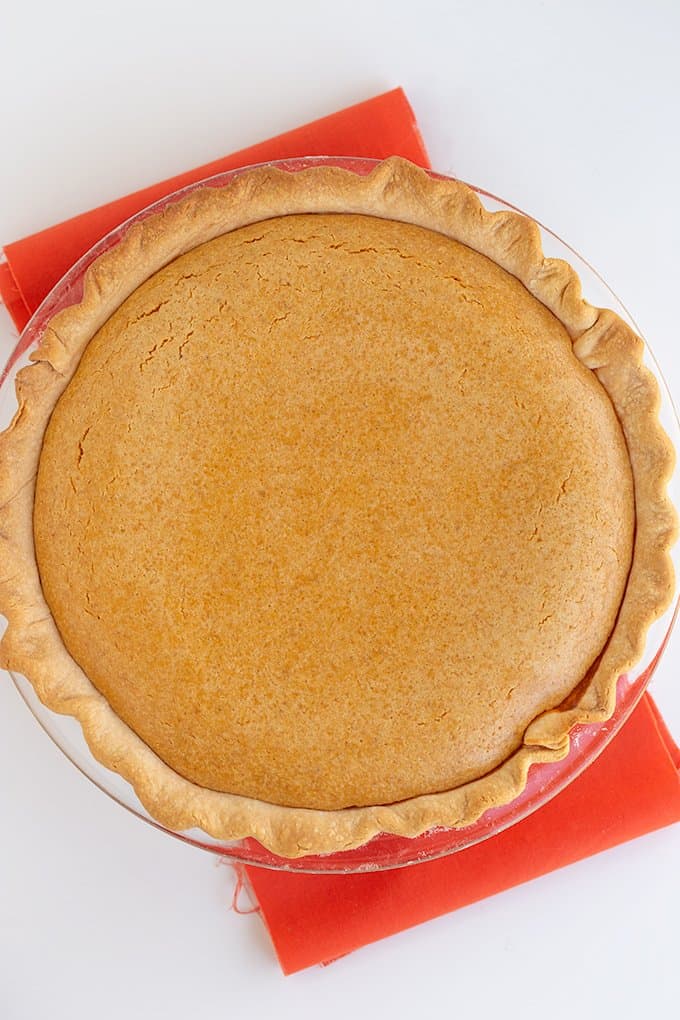 overhead image of a whole cream cheese pumpkin pie on a white surface with an orange fabric