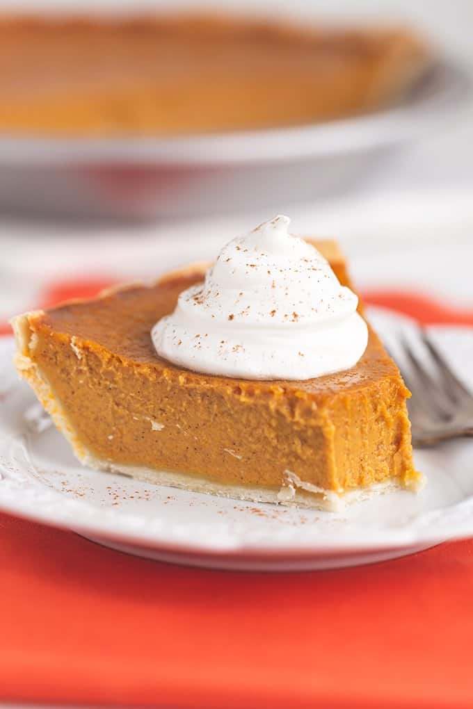 a slice of pie with whipped cream with a bite taken out of it on a white plate with orange fabric 