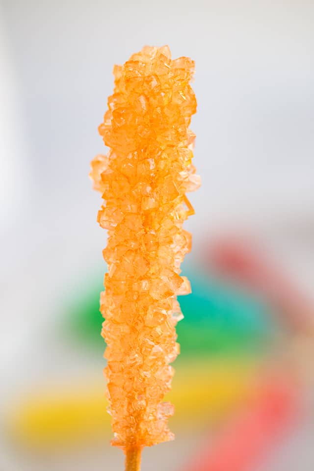 holding rock candy on a stick in front of the plate of rock candy