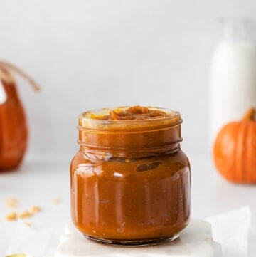 jar of pumpkin butter on white coasters with a gold spoon next to it