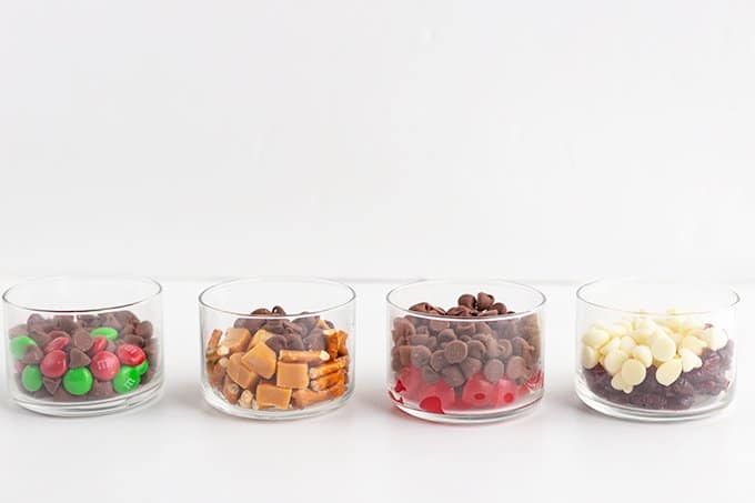 Chocolate chip cookie add-ins in small glass bowls on a white surface