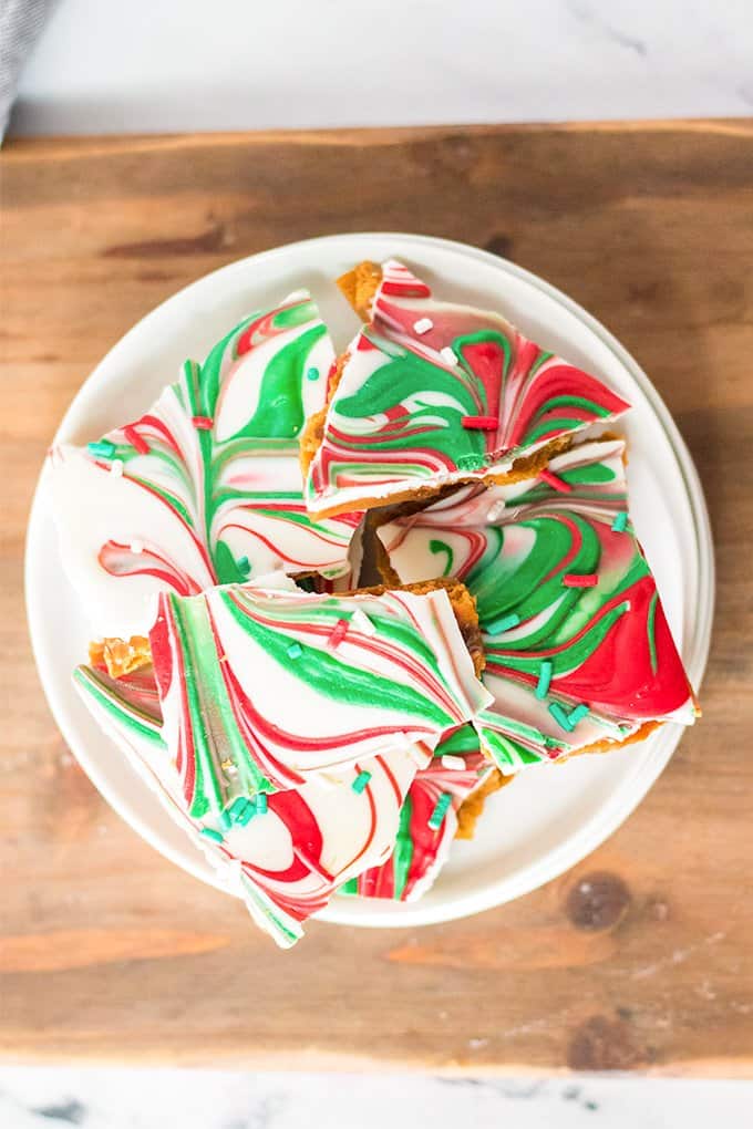 overhead image of the red and green swirled toffee on a white plate on a cutting board and marble surface